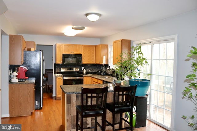 kitchen with sink, backsplash, kitchen peninsula, stainless steel range with electric cooktop, and light wood-type flooring