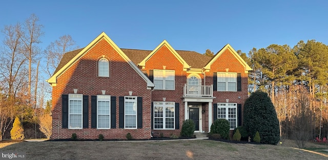 georgian-style home featuring brick siding, a balcony, and a front lawn