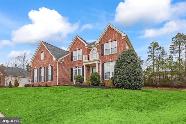 colonial house featuring brick siding, a front yard, and a balcony