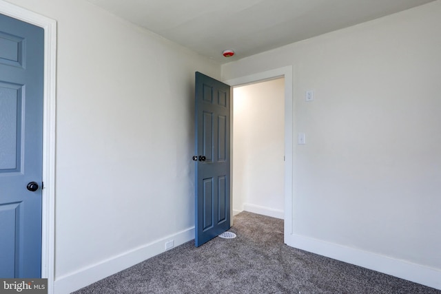 empty room featuring dark colored carpet and baseboards