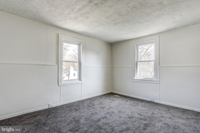 carpeted spare room featuring a wainscoted wall and a textured ceiling