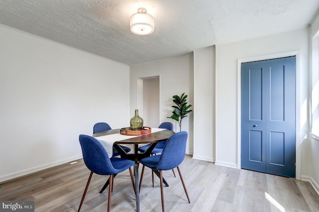 dining room with light wood-type flooring, baseboards, and a textured ceiling