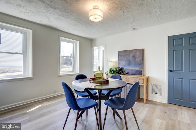 dining space with light wood finished floors, visible vents, a textured ceiling, and baseboards