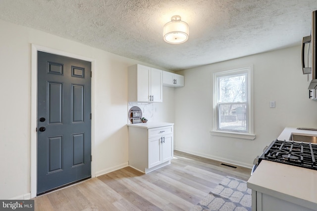 kitchen with light wood finished floors, visible vents, baseboards, light countertops, and white cabinetry