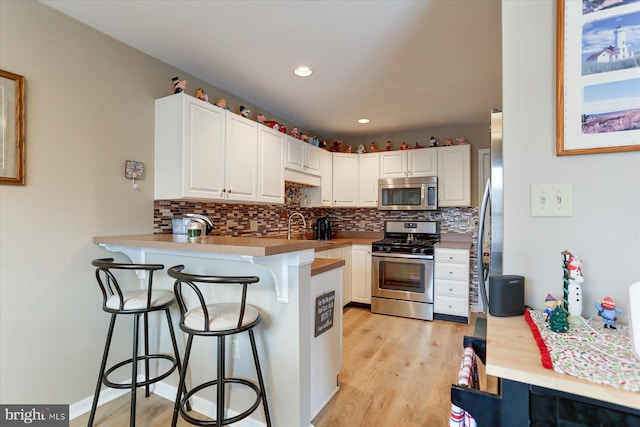 kitchen with white cabinetry, stainless steel appliances, kitchen peninsula, light hardwood / wood-style floors, and a breakfast bar