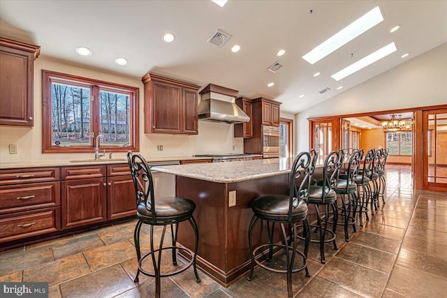 kitchen with sink, a center island, wall chimney range hood, an inviting chandelier, and vaulted ceiling with skylight