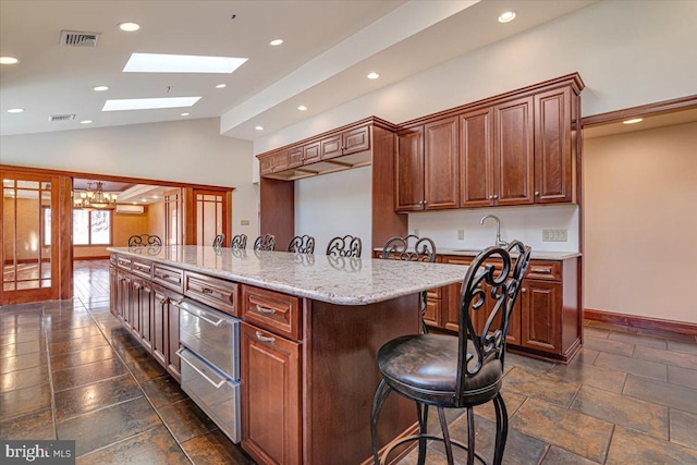 kitchen with light stone countertops, a kitchen breakfast bar, a notable chandelier, a kitchen island with sink, and vaulted ceiling with skylight