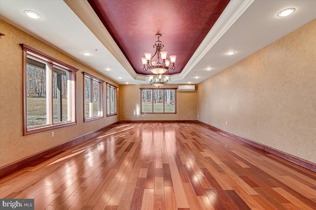 unfurnished dining area with a raised ceiling, crown molding, a notable chandelier, wood-type flooring, and a wall unit AC