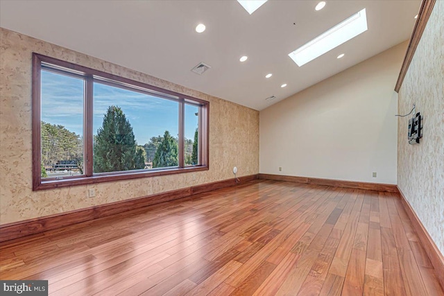 unfurnished room with lofted ceiling with skylight and light hardwood / wood-style flooring