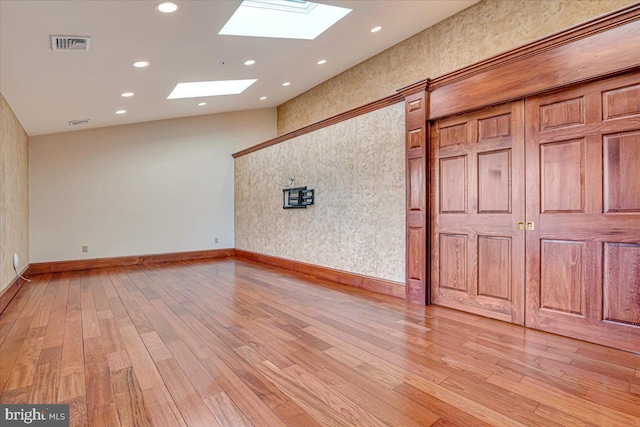 spare room with a skylight and light hardwood / wood-style floors