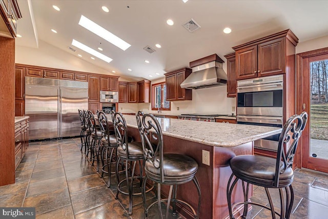 kitchen with lofted ceiling with skylight, a kitchen breakfast bar, built in appliances, wall chimney exhaust hood, and a large island