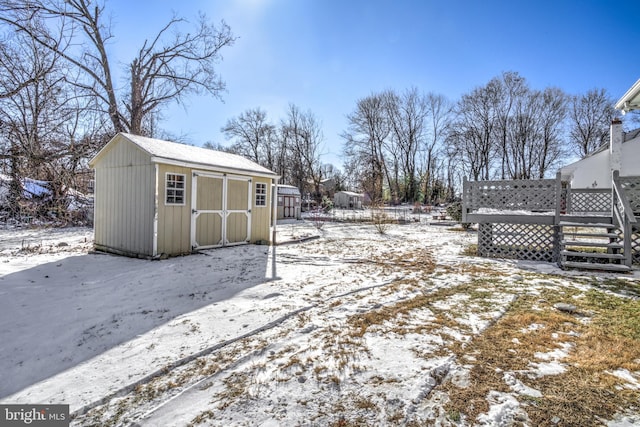 yard layered in snow featuring a wooden deck and a storage shed