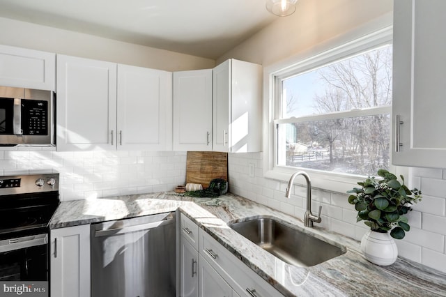 kitchen with backsplash, stainless steel appliances, white cabinetry, and sink