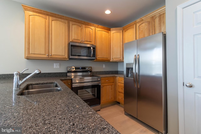 kitchen with appliances with stainless steel finishes, light wood-type flooring, dark stone counters, and sink