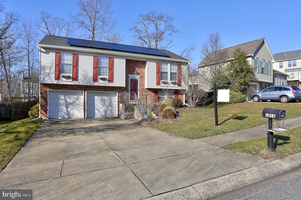 raised ranch featuring solar panels, a front yard, and a garage