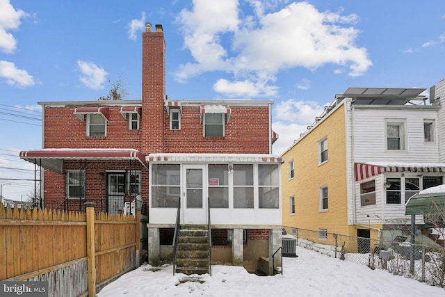 snow covered back of property with central AC and a sunroom