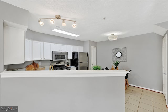 kitchen featuring kitchen peninsula, appliances with stainless steel finishes, a textured ceiling, light tile patterned floors, and white cabinetry