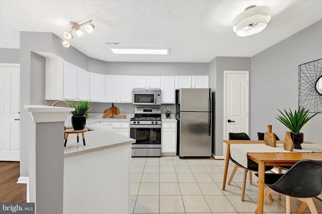 kitchen featuring appliances with stainless steel finishes, light tile patterned floors, a textured ceiling, and white cabinetry