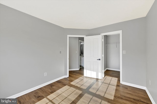 unfurnished bedroom featuring a walk in closet, wood-type flooring, and a closet