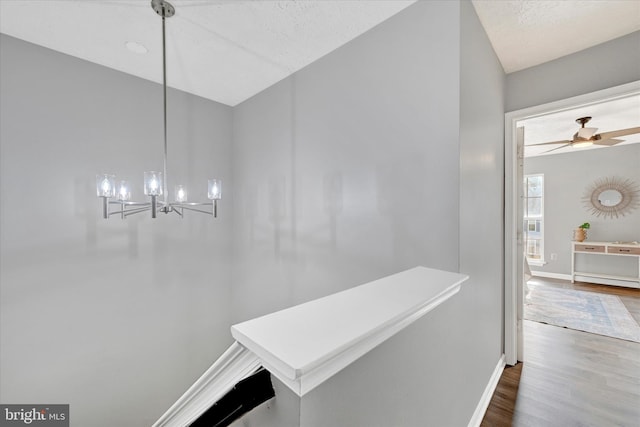 corridor featuring a chandelier, wood-type flooring, and a textured ceiling