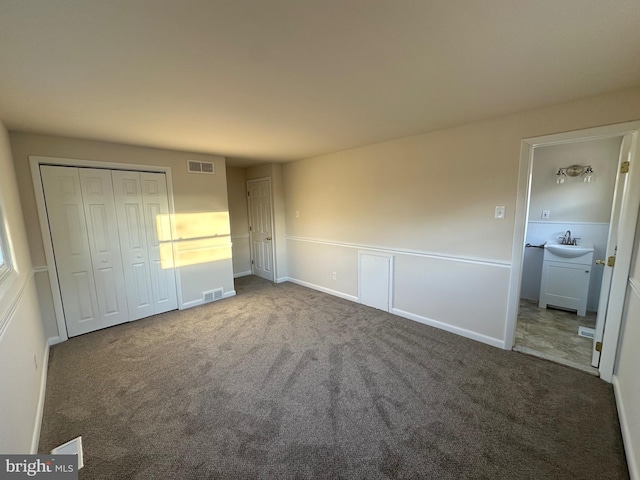 unfurnished bedroom with a closet, ensuite bathroom, sink, and dark colored carpet