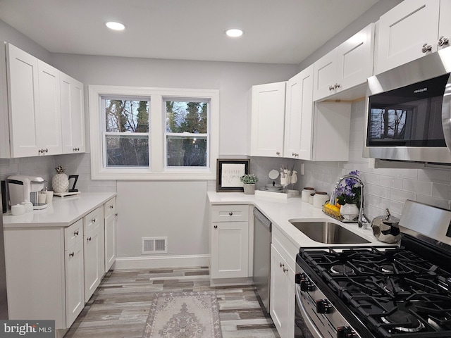 kitchen with light wood-type flooring, stainless steel appliances, white cabinetry, and sink