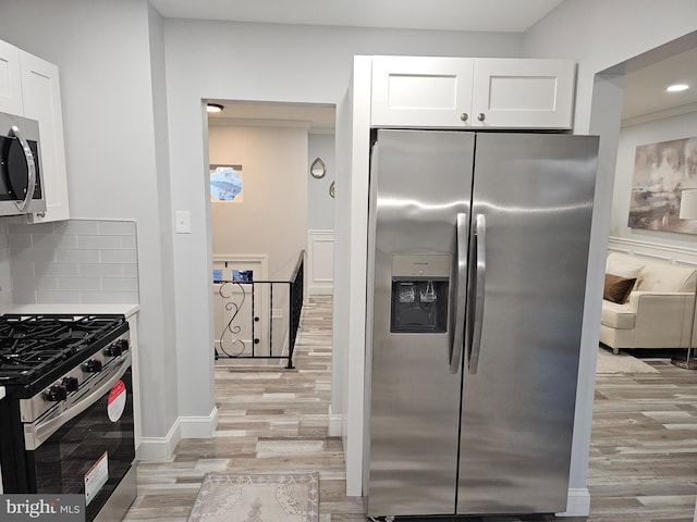 kitchen with appliances with stainless steel finishes, light hardwood / wood-style floors, white cabinetry, and tasteful backsplash