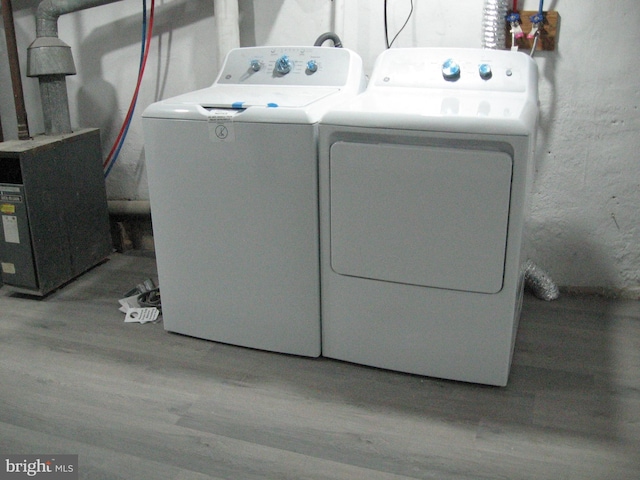 clothes washing area featuring heating unit, hardwood / wood-style floors, and washer and dryer