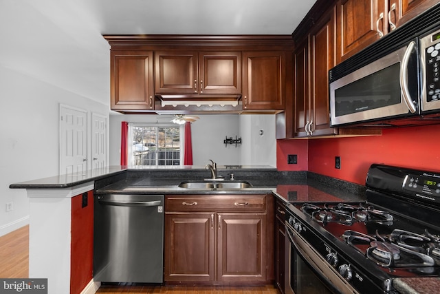 kitchen featuring sink, light hardwood / wood-style flooring, appliances with stainless steel finishes, kitchen peninsula, and dark stone counters