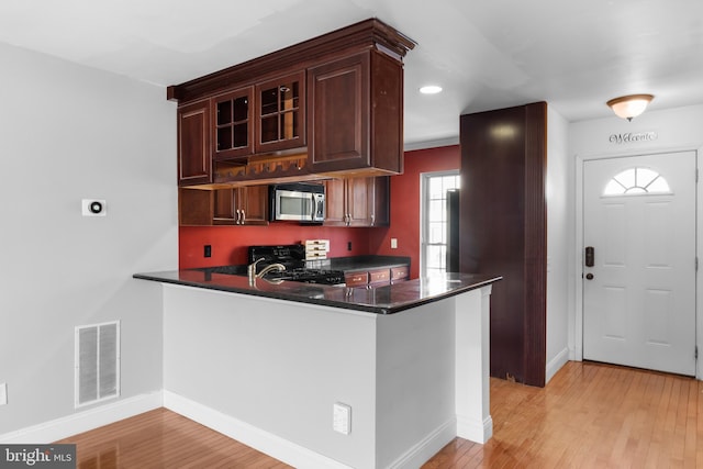 kitchen with dark stone countertops, kitchen peninsula, light hardwood / wood-style floors, and stove