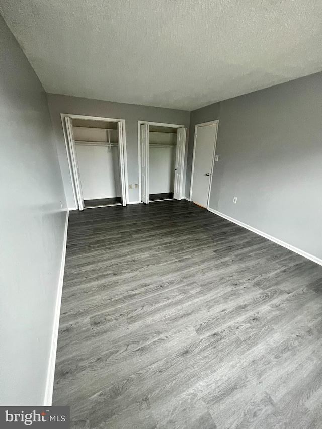 unfurnished bedroom featuring dark hardwood / wood-style floors, a textured ceiling, and two closets