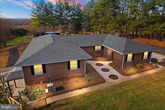 ranch-style house featuring brick siding, a yard, a shingled roof, driveway, and a fire pit