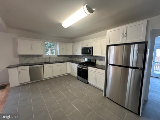 kitchen with white cabinetry, sink, backsplash, dark tile patterned flooring, and appliances with stainless steel finishes