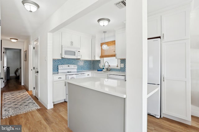 kitchen with white appliances, white cabinets, hanging light fixtures, light wood-type flooring, and tasteful backsplash