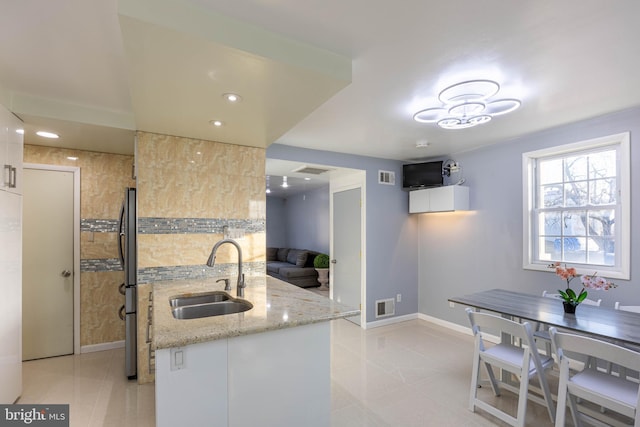 kitchen featuring stainless steel fridge, light stone counters, sink, light tile patterned floors, and white cabinetry