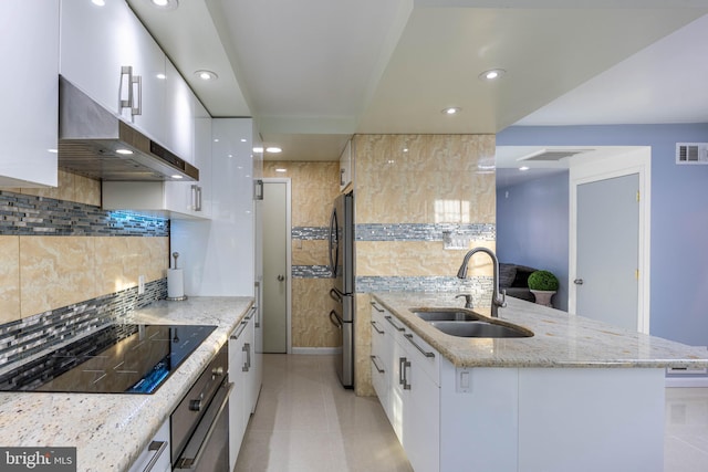 kitchen featuring wall chimney exhaust hood, sink, white cabinets, and black electric stovetop