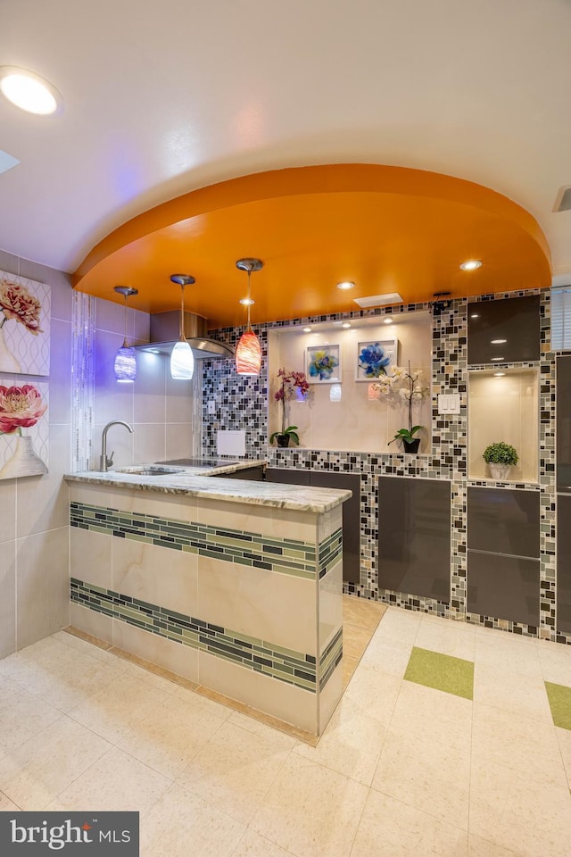 kitchen with tile patterned flooring, decorative light fixtures, sink, and tile walls