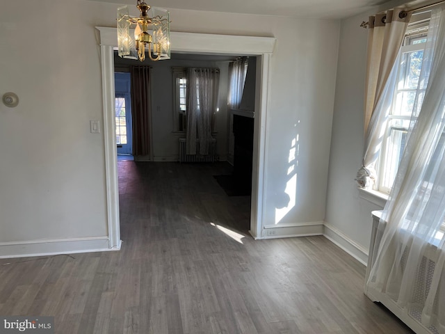 unfurnished dining area with radiator heating unit, hardwood / wood-style floors, and a notable chandelier