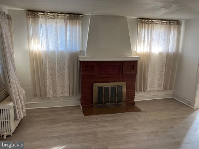 unfurnished living room featuring a fireplace, wood-type flooring, and radiator heating unit