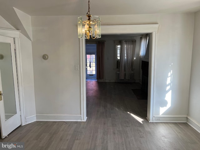 unfurnished dining area with a notable chandelier, dark wood-type flooring, and radiator