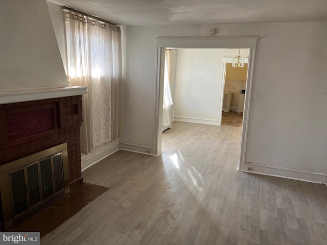 unfurnished living room featuring a fireplace, light hardwood / wood-style flooring, and an inviting chandelier