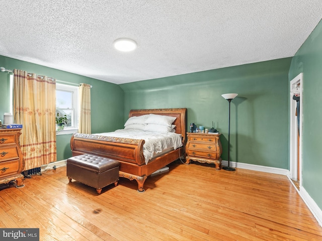 bedroom featuring lofted ceiling, light hardwood / wood-style floors, and a textured ceiling