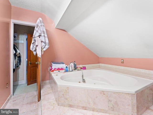 bathroom featuring a textured ceiling, vaulted ceiling, and tiled tub