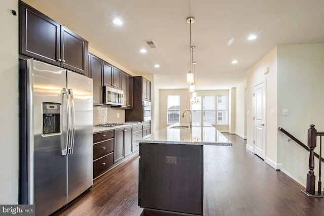 kitchen featuring light stone counters, dark brown cabinets, hanging light fixtures, a center island with sink, and stainless steel appliances