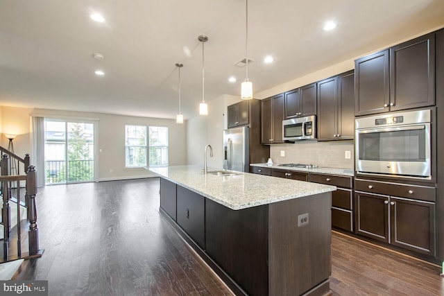 kitchen with sink, dark brown cabinets, hanging light fixtures, appliances with stainless steel finishes, and a kitchen island with sink