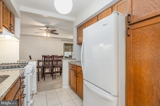 kitchen with light stone countertops, light tile patterned floors, white appliances, and ceiling fan