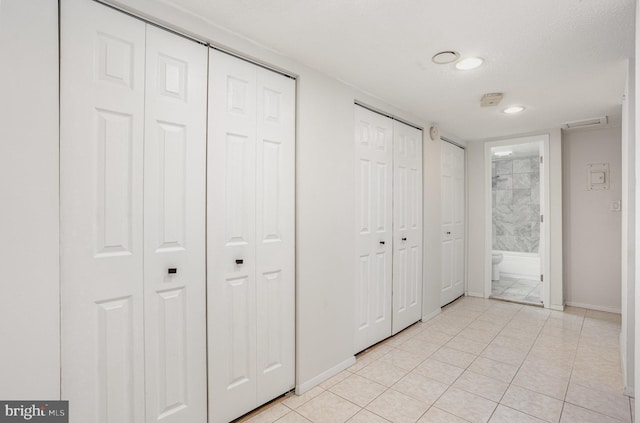 interior space featuring a textured ceiling, connected bathroom, light tile patterned floors, and two closets