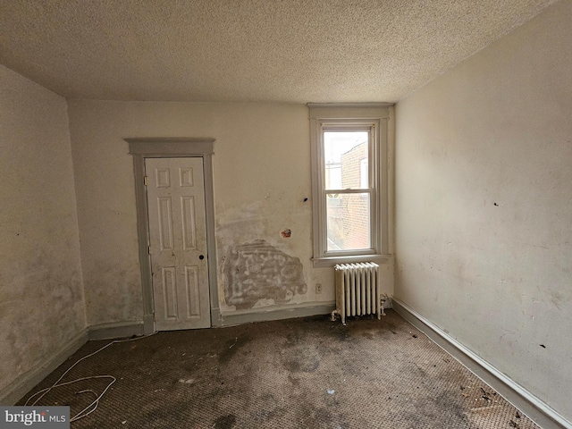 carpeted empty room with radiator heating unit and a textured ceiling