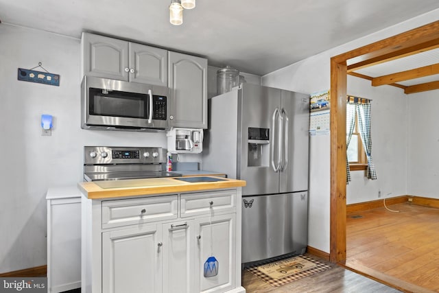 kitchen featuring beamed ceiling, appliances with stainless steel finishes, white cabinetry, and hardwood / wood-style floors