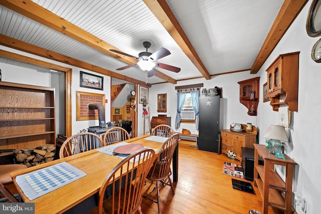 dining space with beamed ceiling, ceiling fan, light wood-type flooring, and a wood stove